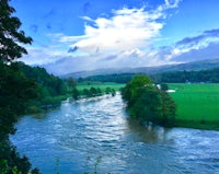 a river running through a green field with a cloudy sky
